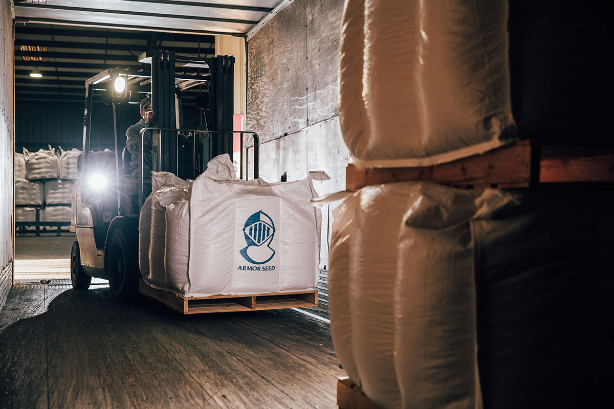 a forklift loading a pallet of seed into a trailer